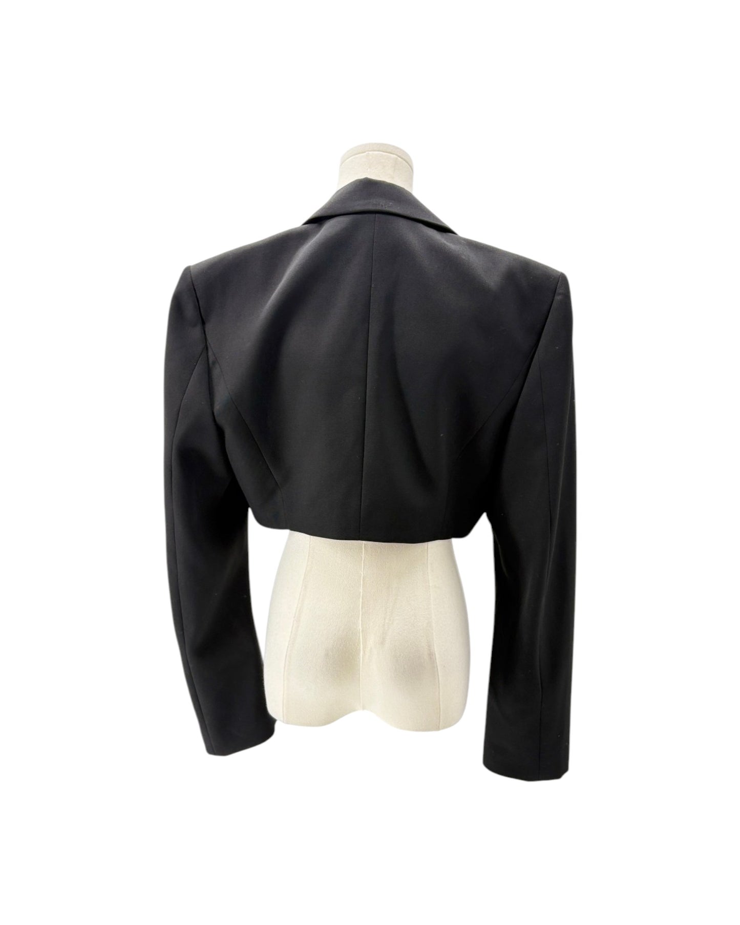 A black cropped blazer with long sleeves and a structured collar, shown from the back on a cream-colored mannequin torso against a white background.
