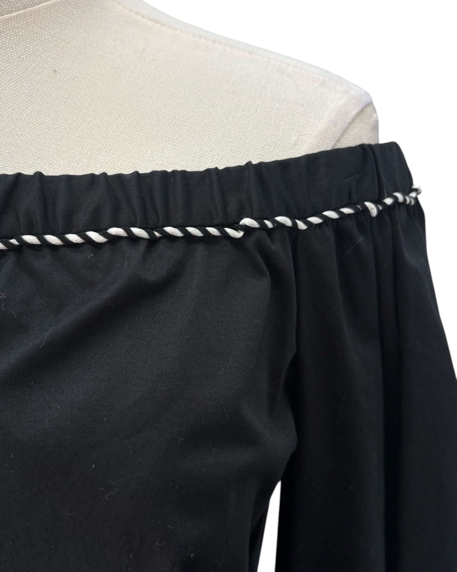 Black off-shoulder top with white trim on a mannequin against a white background