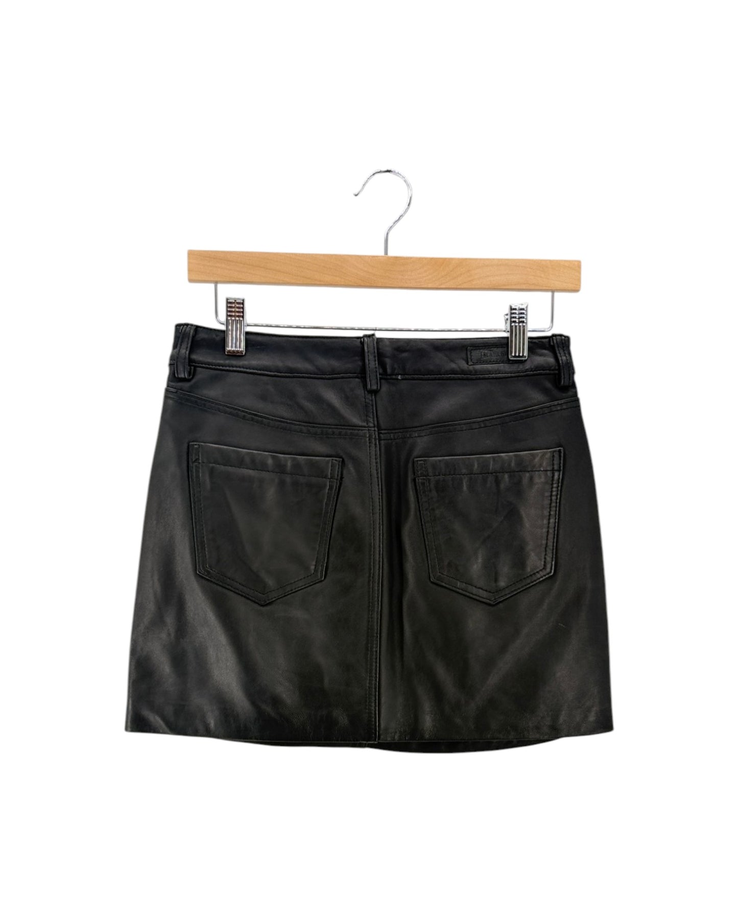Black faux leather mini skirt with two large back patch pockets, hanging on a wooden hanger against a white background.