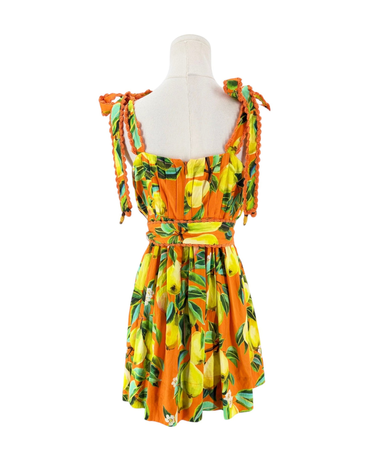 An orange sleeveless dress with a yellow and green lemon print, featuring tie-shoulder straps, a smocked bodice, and a matching orange belt with a round buckle, displayed on a white mannequin torso against a white background.