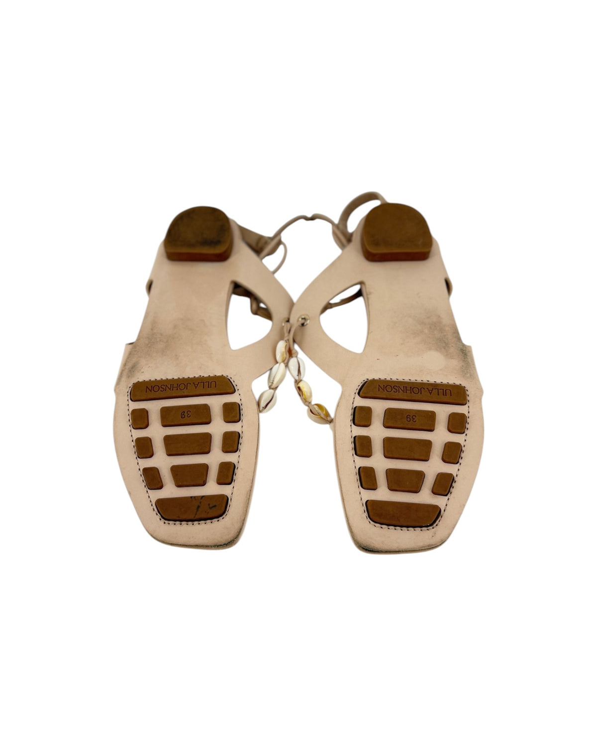 A pair of leather thong sandal soles with long leather ankle wrap straps and seashell details on a white background