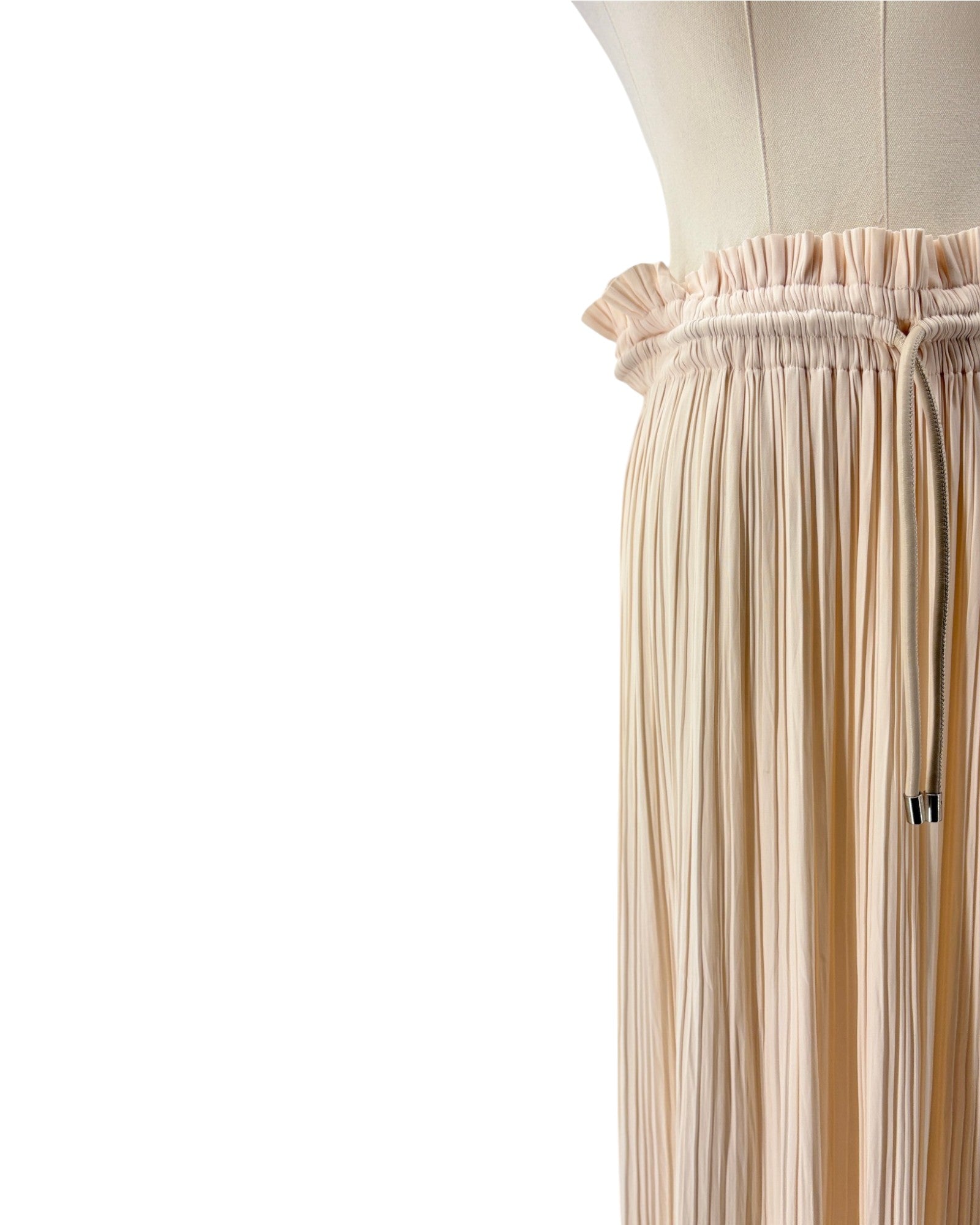 Close-up of a pleated skirt in a light beige or cream color, displayed on a dress form against a white background.