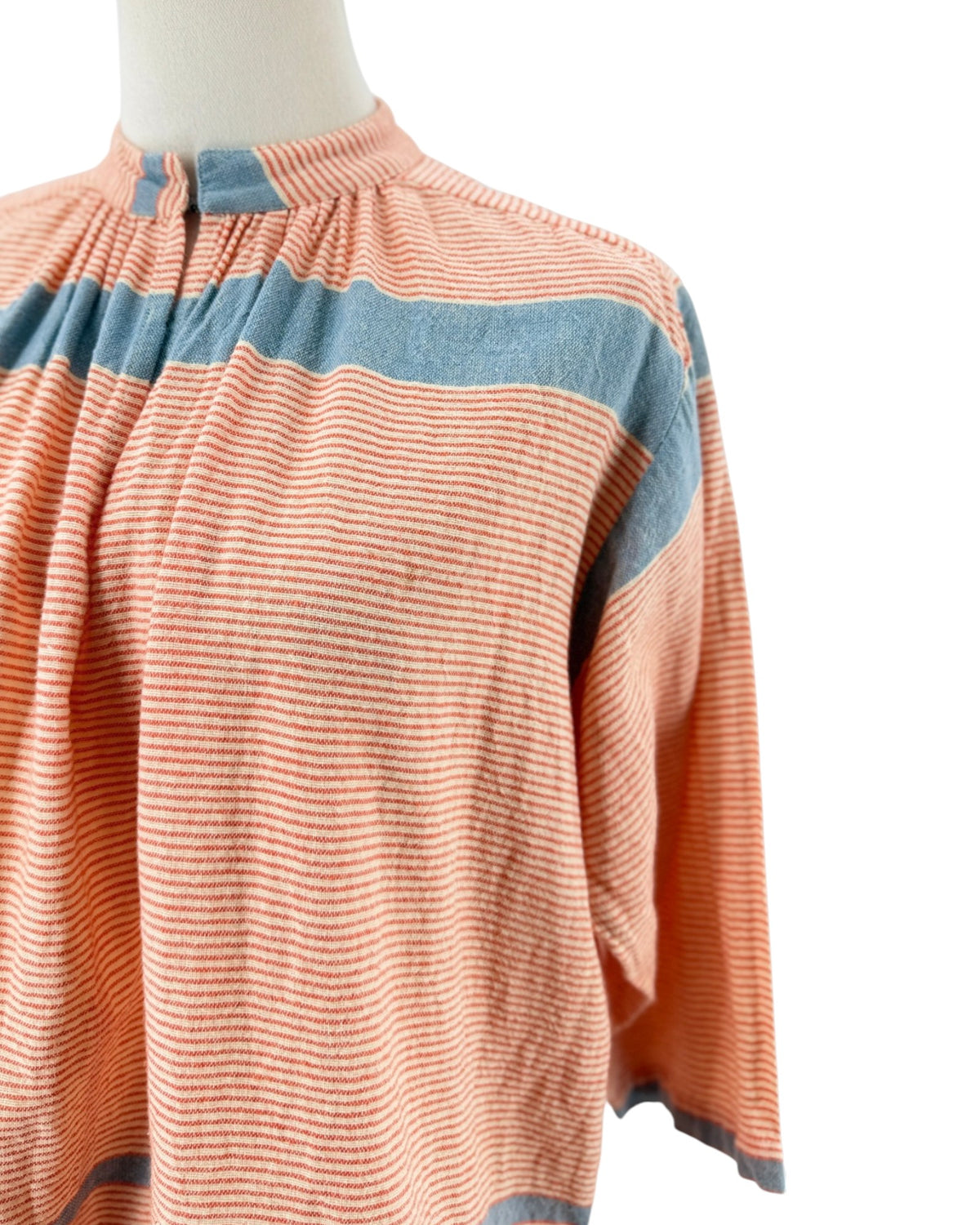 A peach-colored long-sleeve blouse with blue horizontal stripes, displayed on a mannequin torso against a white background.