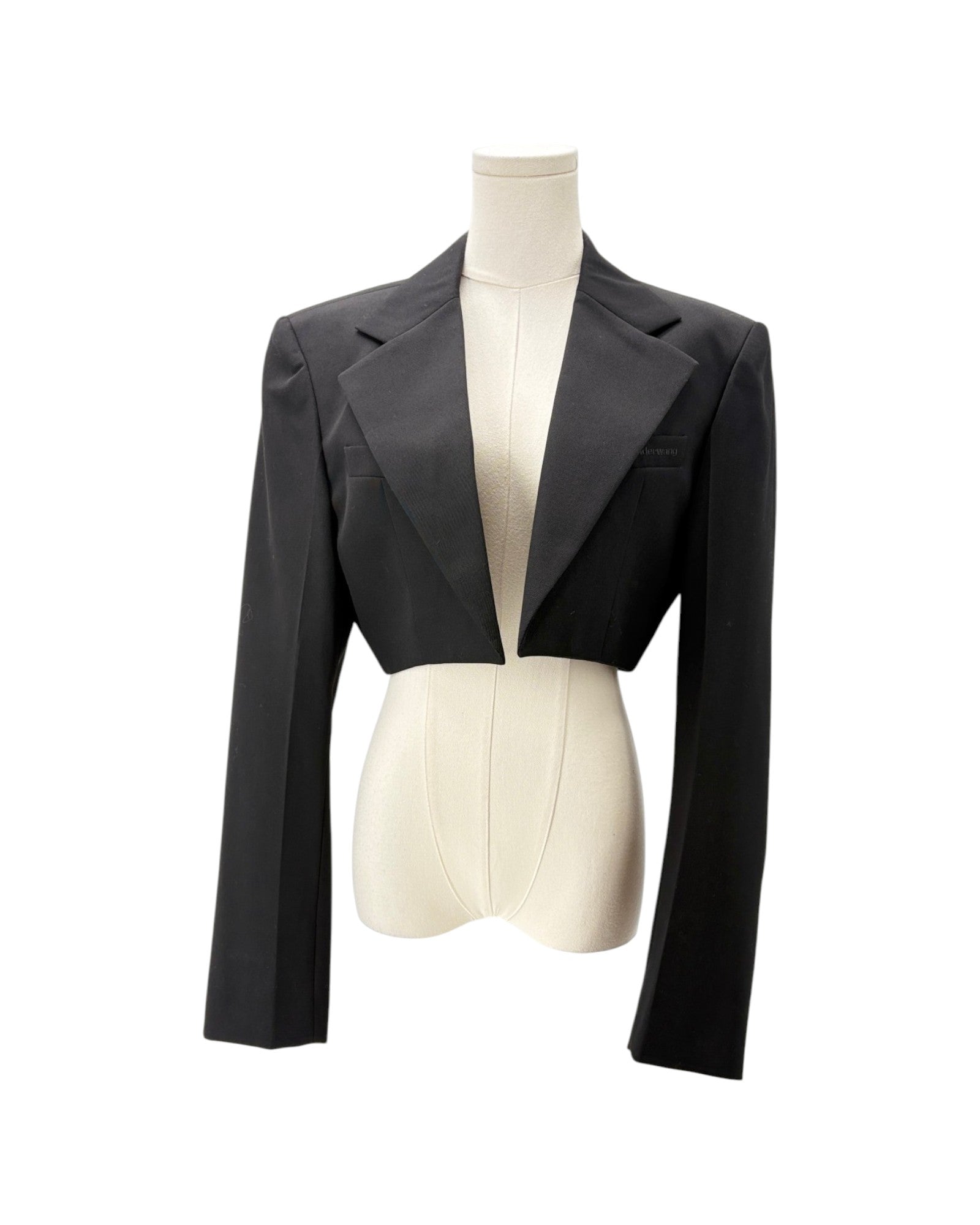 A black cropped blazer with structured shoulders and long sleeves, displayed on a cream-colored mannequin torso against a plain white background.