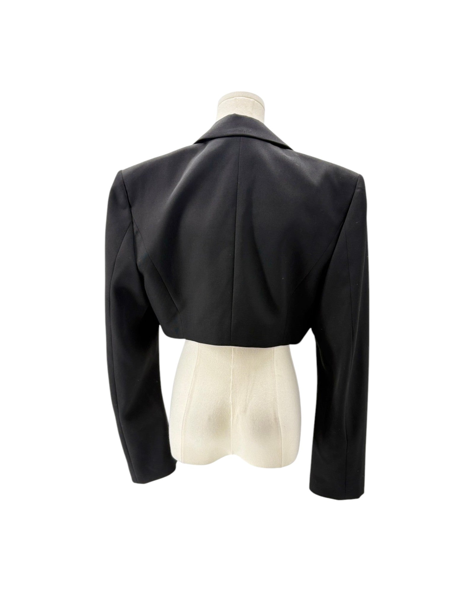 A black cropped blazer with long sleeves and a structured collar, shown from the back on a cream-colored mannequin torso against a white background.