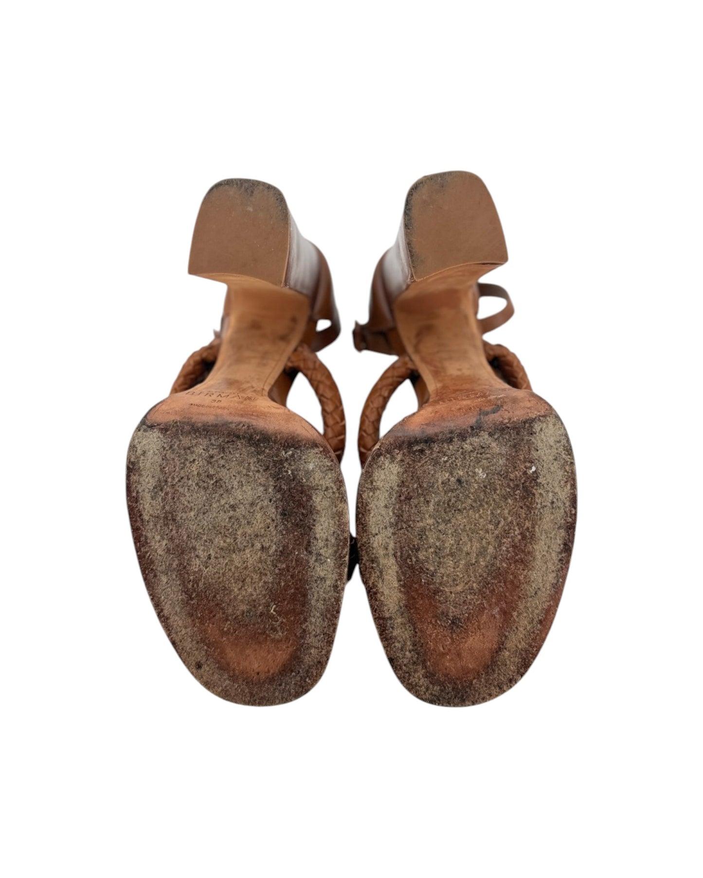 A pair of women's strappy sandals shown from the sole view, featuring a light beige upper and a heavily scuffed, worn brown rubber sole, set against a plain white background.