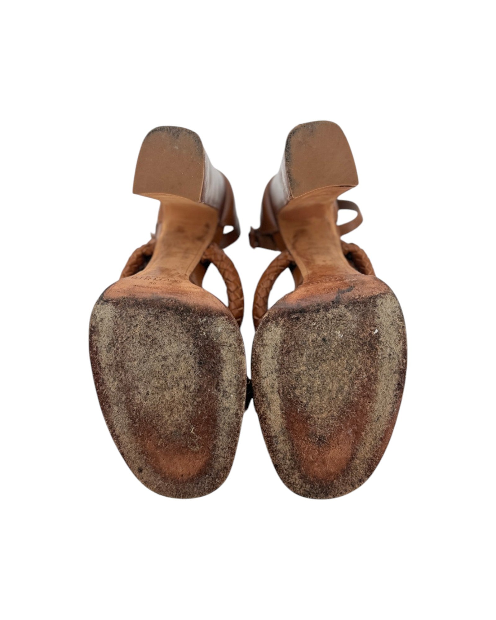 A pair of women's strappy sandals shown from the sole view, featuring a light beige upper and a heavily scuffed, worn brown rubber sole, set against a plain white background.