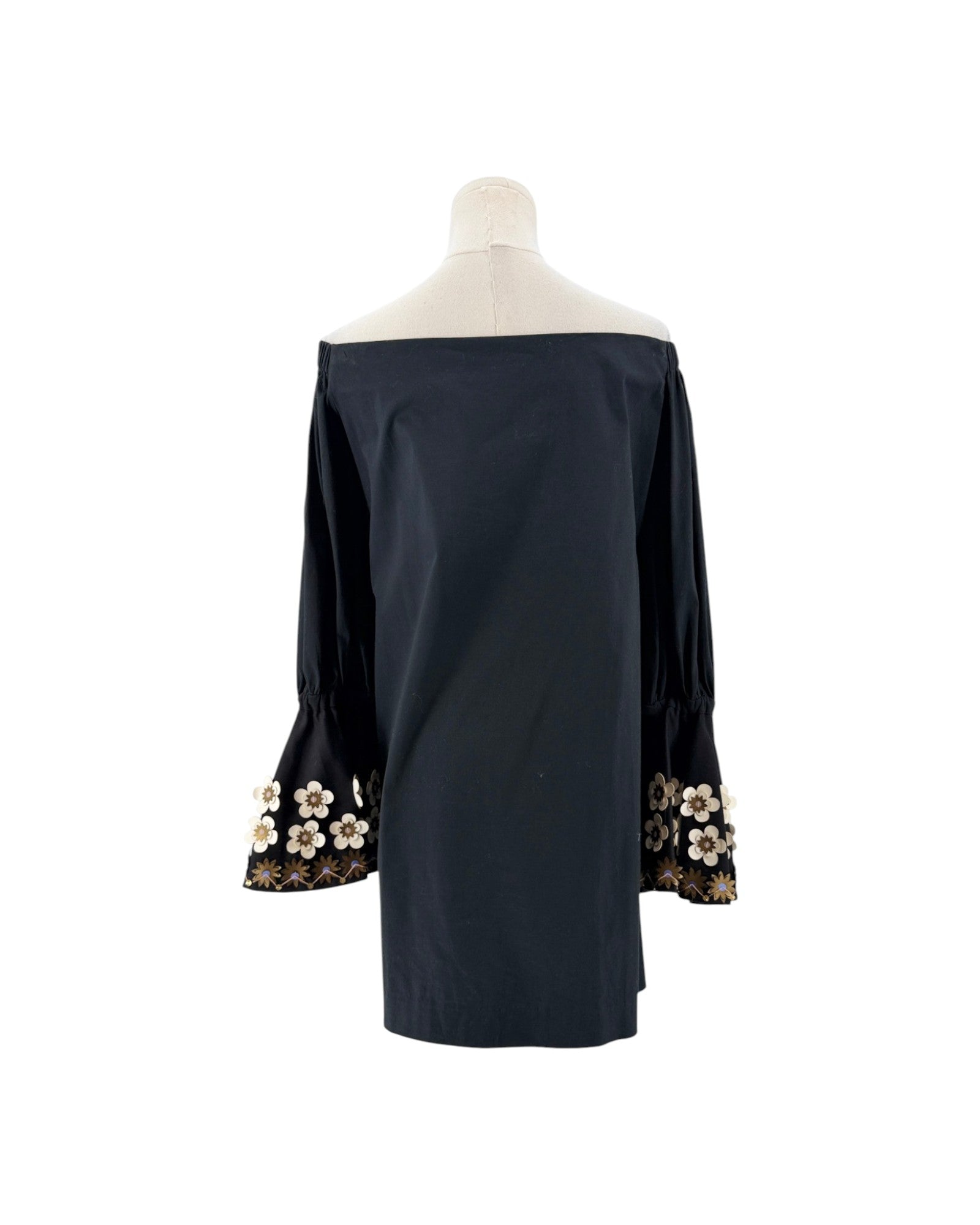 A black off-the-shoulder long-sleeve blouse displayed on a mannequin torso, featuring decorative floral lace and bead trim at the cuffs.