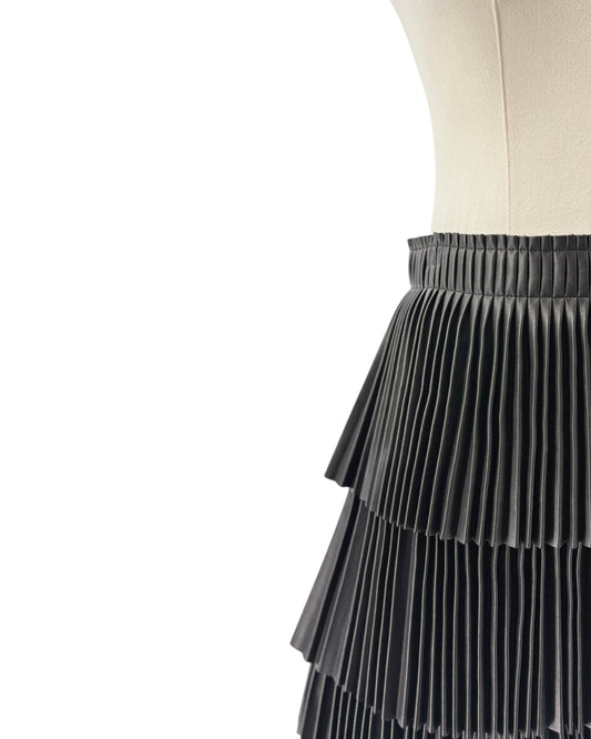 A close-up of a black pleated skirt displayed on a cream dress form against a white background.