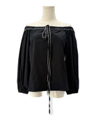 Black off-shoulder blouse with white trim on a mannequin against a white background