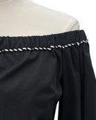 Black off-shoulder top with white trim on a mannequin against a white background