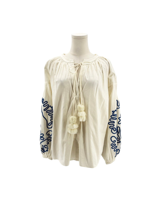 An off-white or cream-colored blouse with dramatic puffed sleeves, featuring dark blue embroidered floral and script patterns on the sleeves, displayed on a mannequin against a white background.