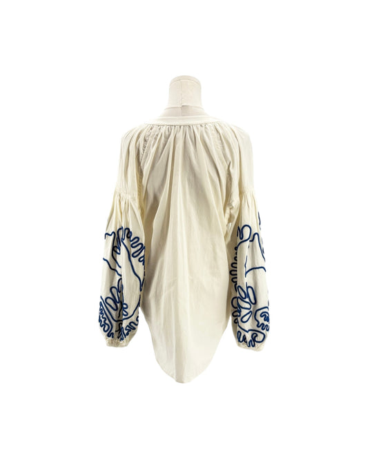 An off-white or cream-colored blouse with dramatic puffed sleeves, featuring dark blue embroidered floral and script patterns on the sleeves, displayed on a mannequin against a white background.