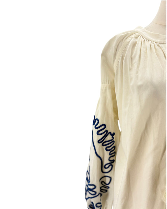 An off-white long-sleeve blouse with dark blue cursive embroidery on the sleeve, shown on a mannequin against a plain white background.