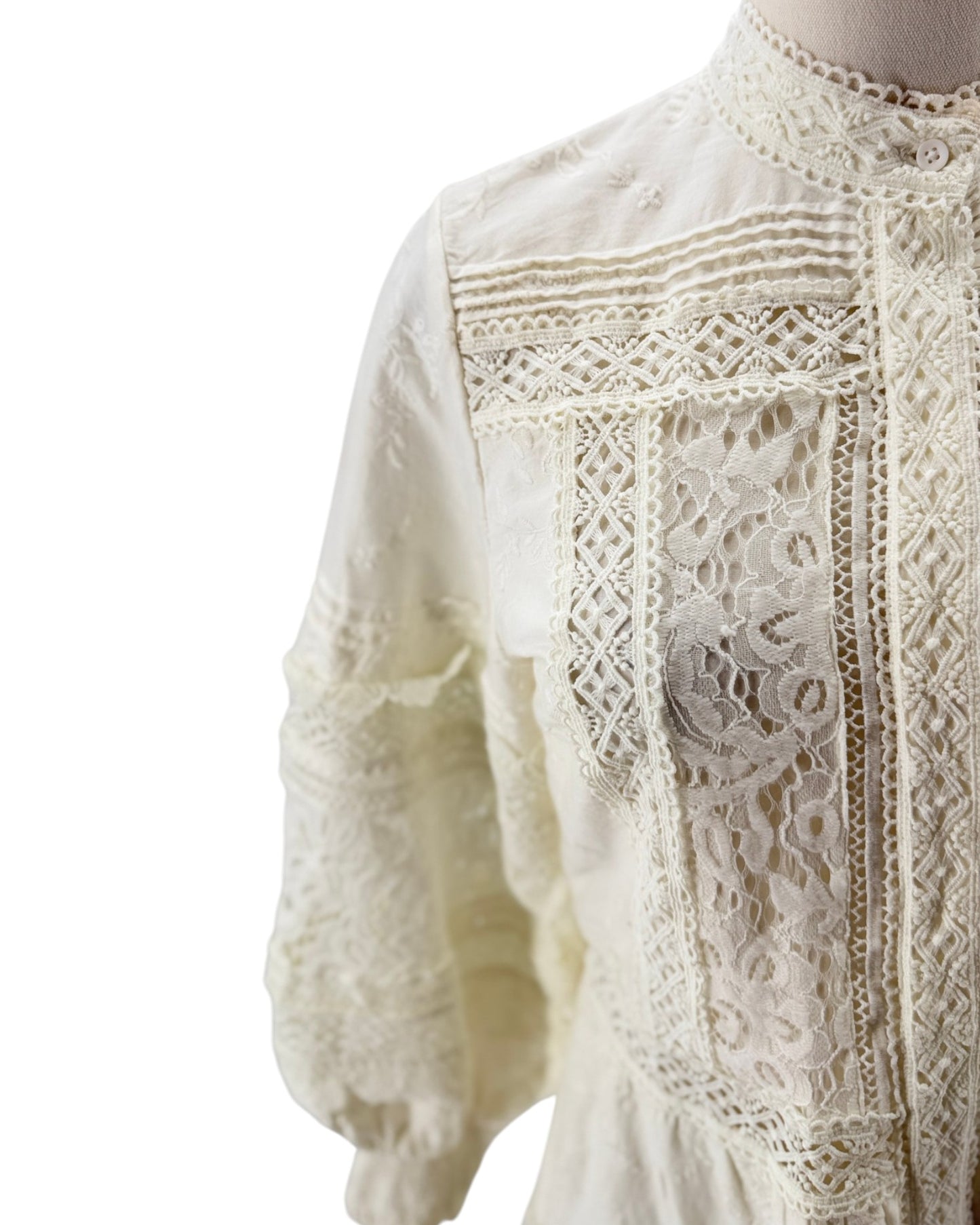 Close-up of a white lace blouse on a mannequin against a white background