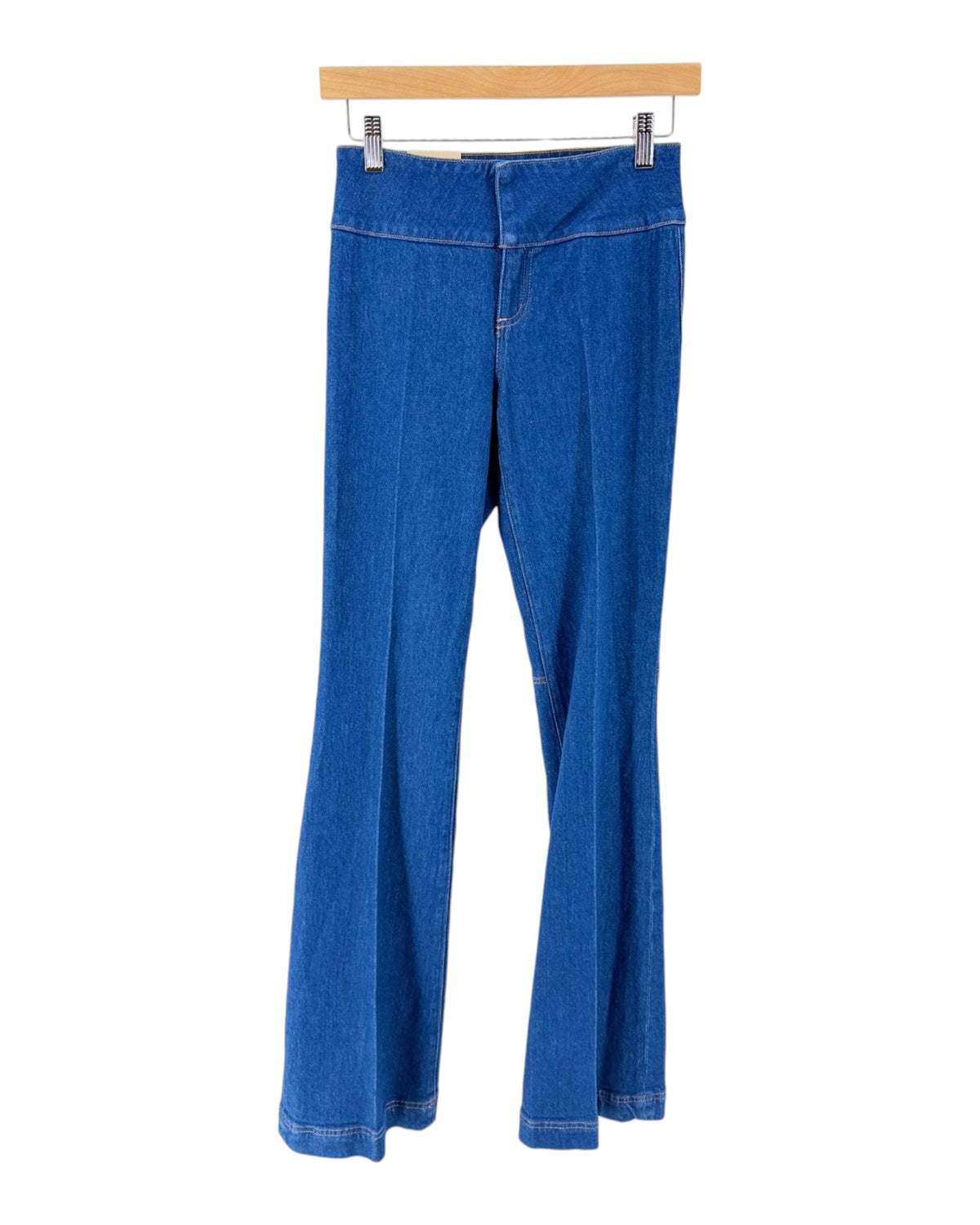 Medium wash blue denim flare jeans hanging from a light wood hanger against a plain white background.