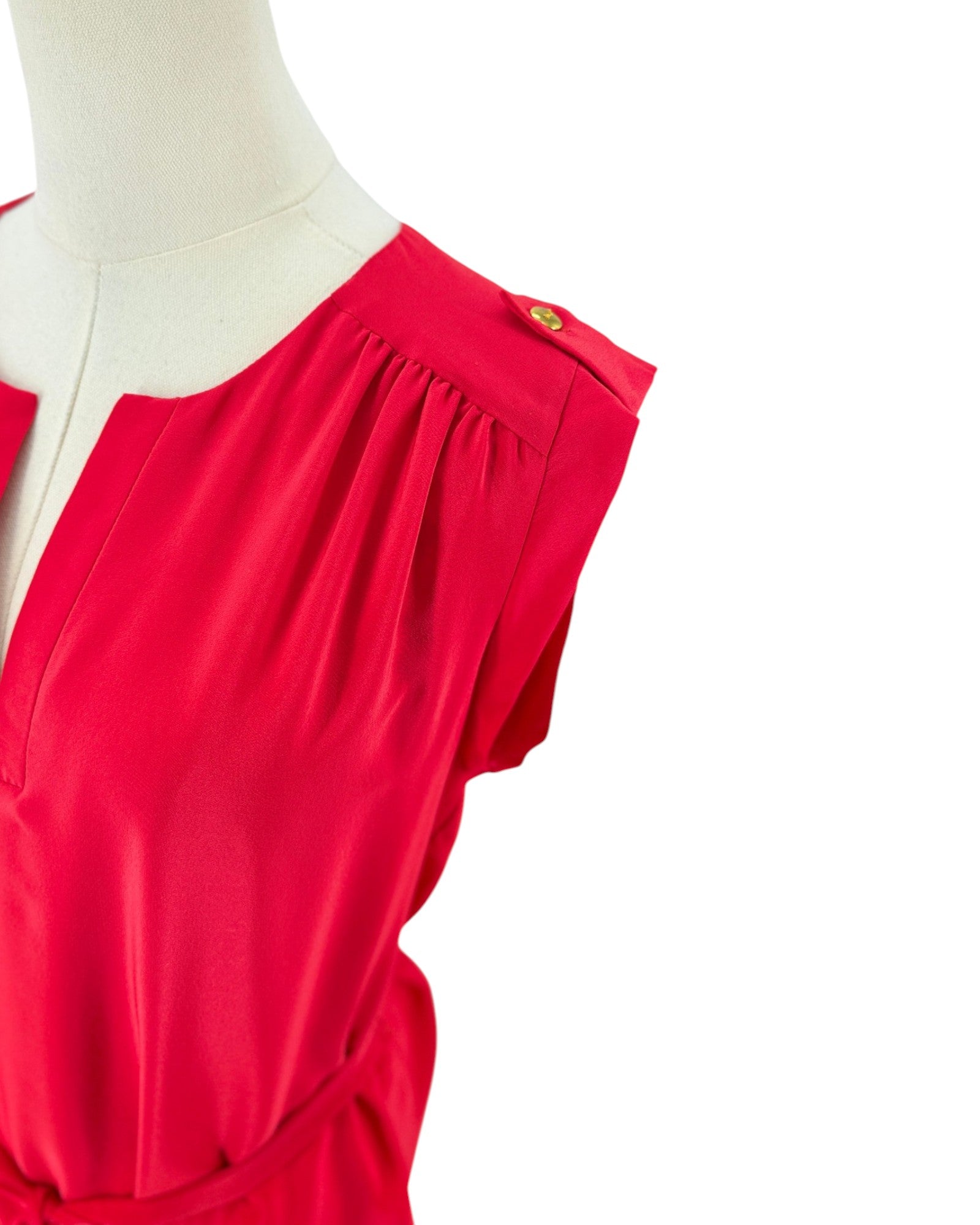 A close-up of a bright red dress or top displayed on a cream mannequin torso against a white background, showing a gathered shoulder detail and a small gold button accent.