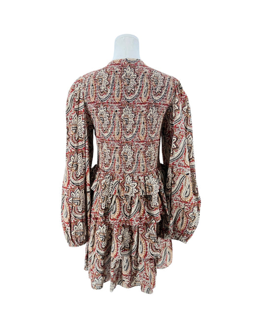 A long-sleeve mini dress with a deep V-neck and a busy paisley pattern in red, beige, and black, displayed on a white mannequin torso against a plain white background.