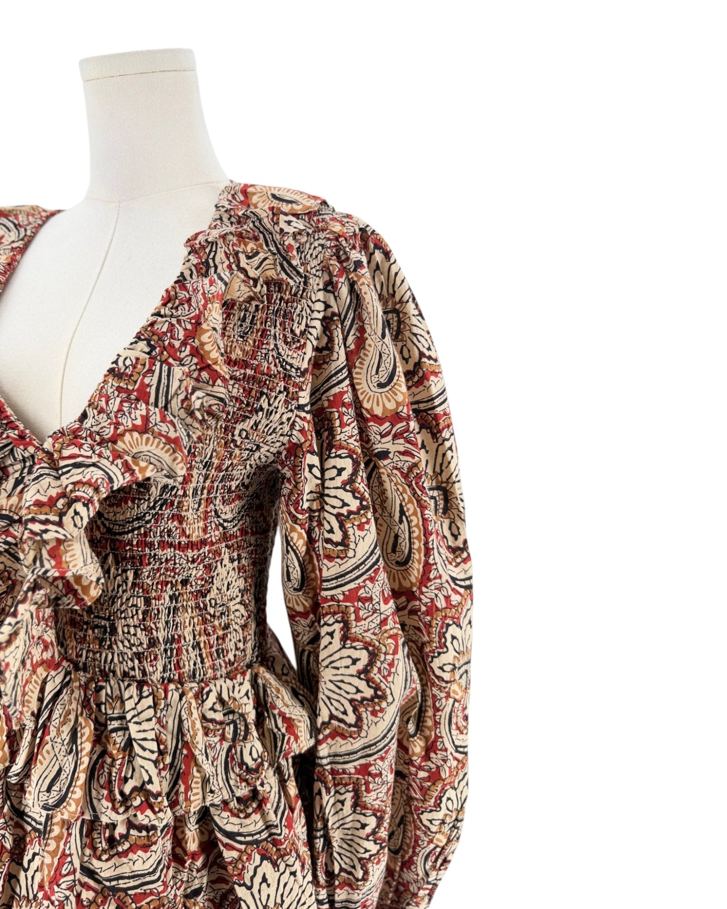 A long-sleeve mini dress with a deep V-neck and a busy paisley pattern in red, beige, and black, displayed on a white mannequin torso against a plain white background.