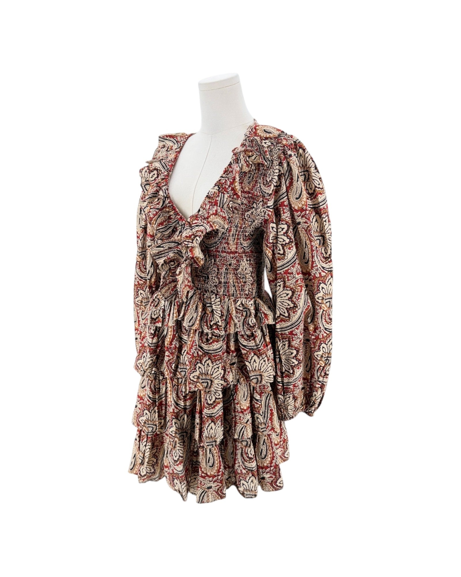 A long-sleeve mini dress with a deep V-neck and a busy paisley pattern in red, beige, and black, displayed on a white mannequin torso against a plain white background.