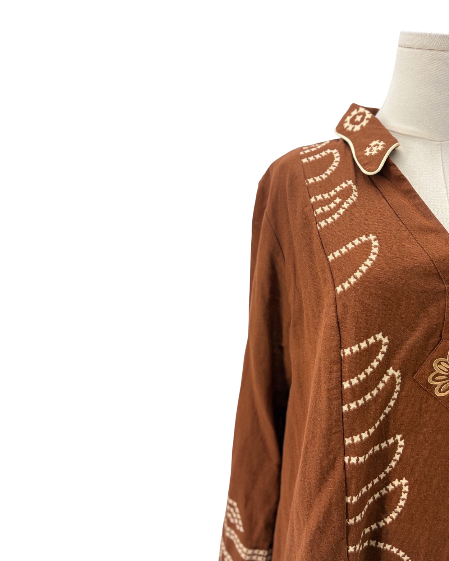 Brown dress with white embroidery on a mannequin against a white background