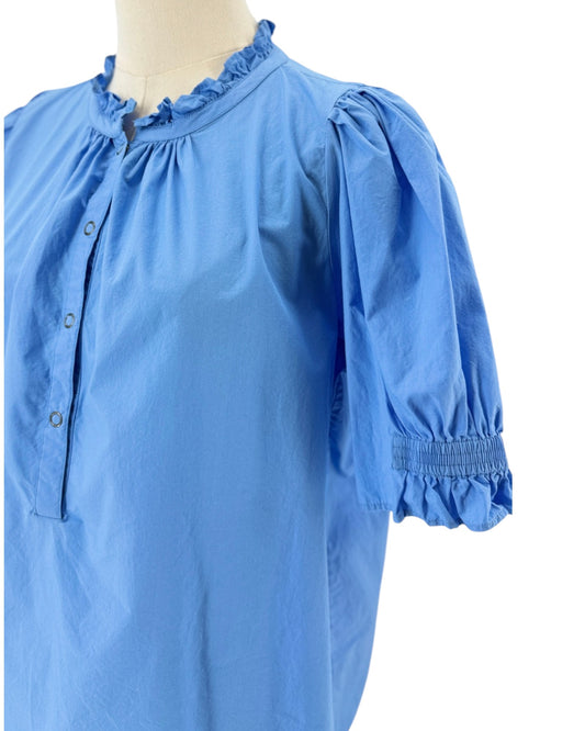 A light blue blouse displayed on a mannequin torso, featuring a ruffled mock neck, buttoned henley front, puff sleeves with smocked cuffs, and a gathered waist.