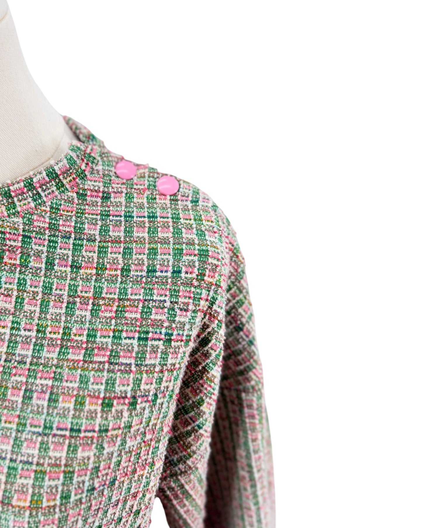 A close-up of a tweed jacket on a mannequin, featuring a green, pink, and white checkered pattern with two pink buttons at the collar, set against a plain white background.