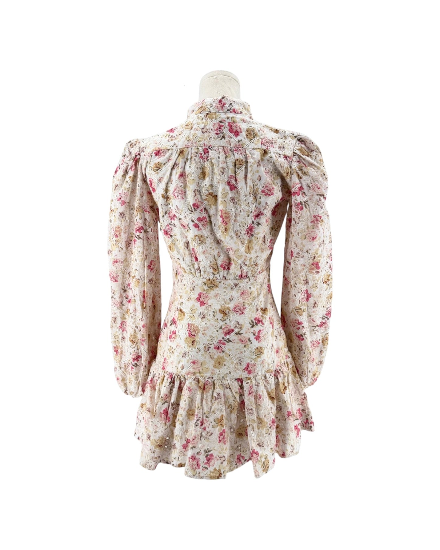 A long-sleeve floral dress displayed on a mannequin from the back, featuring a cream base with pink, red, and green floral patterns and a ruffled hem.