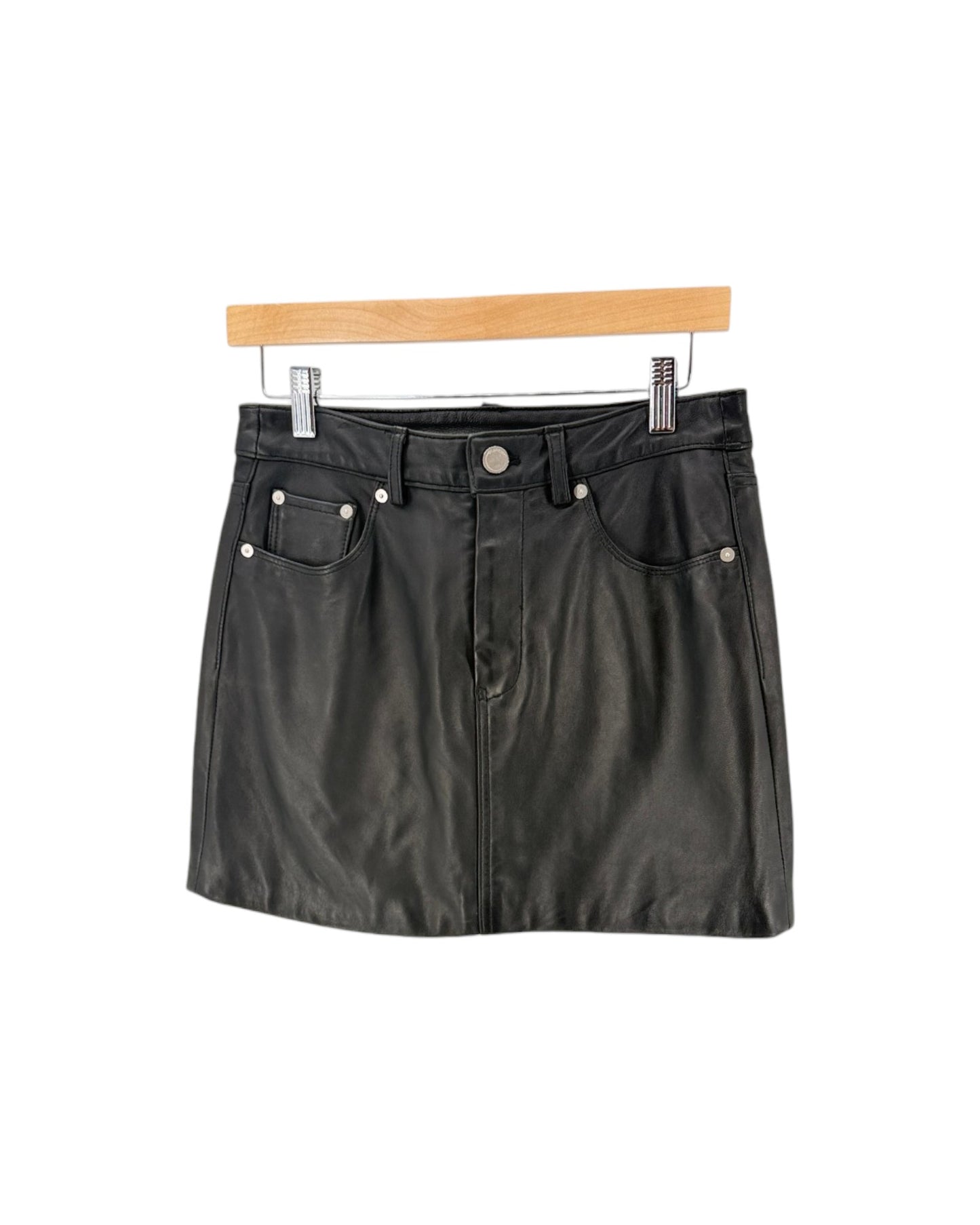 A black faux-leather mini skirt with silver rivets and a button closure, hanging from a wooden hanger against a white background.