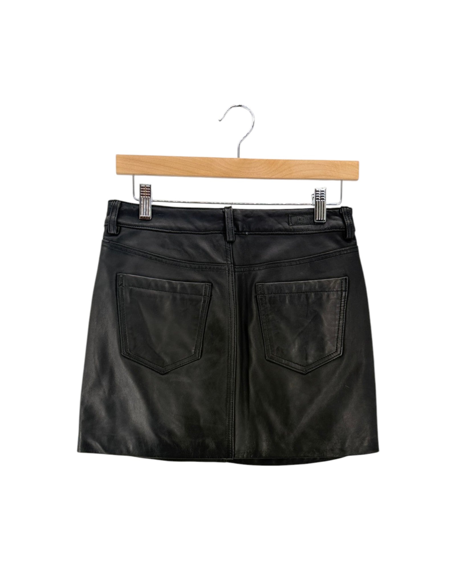 Black faux leather mini skirt with two large back patch pockets, hanging on a wooden hanger against a white background.