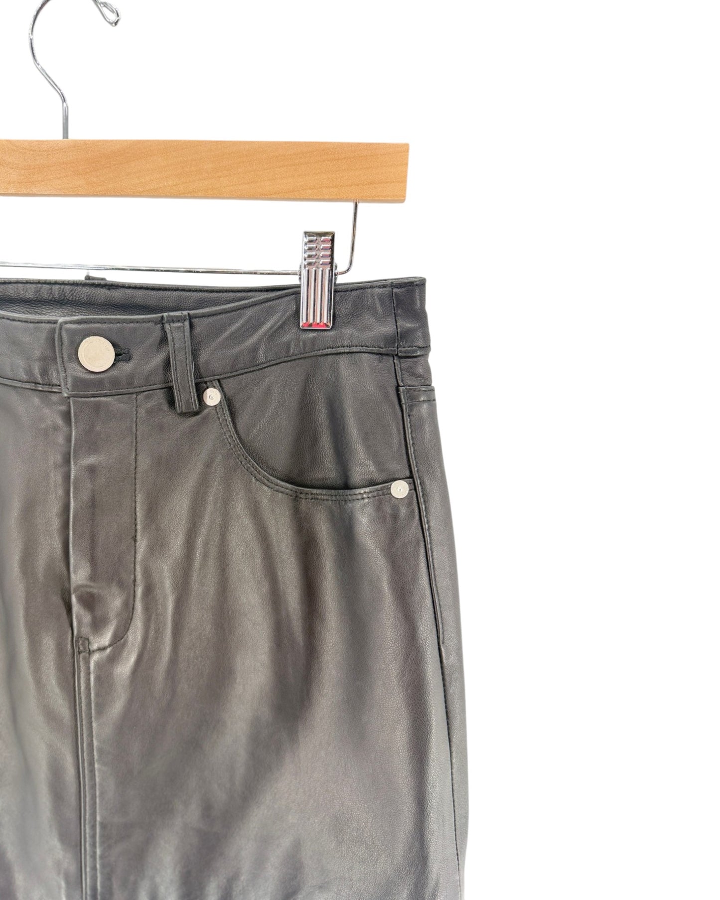 Close-up of dark gray leather pants hanging on a wooden hanger against a white background.