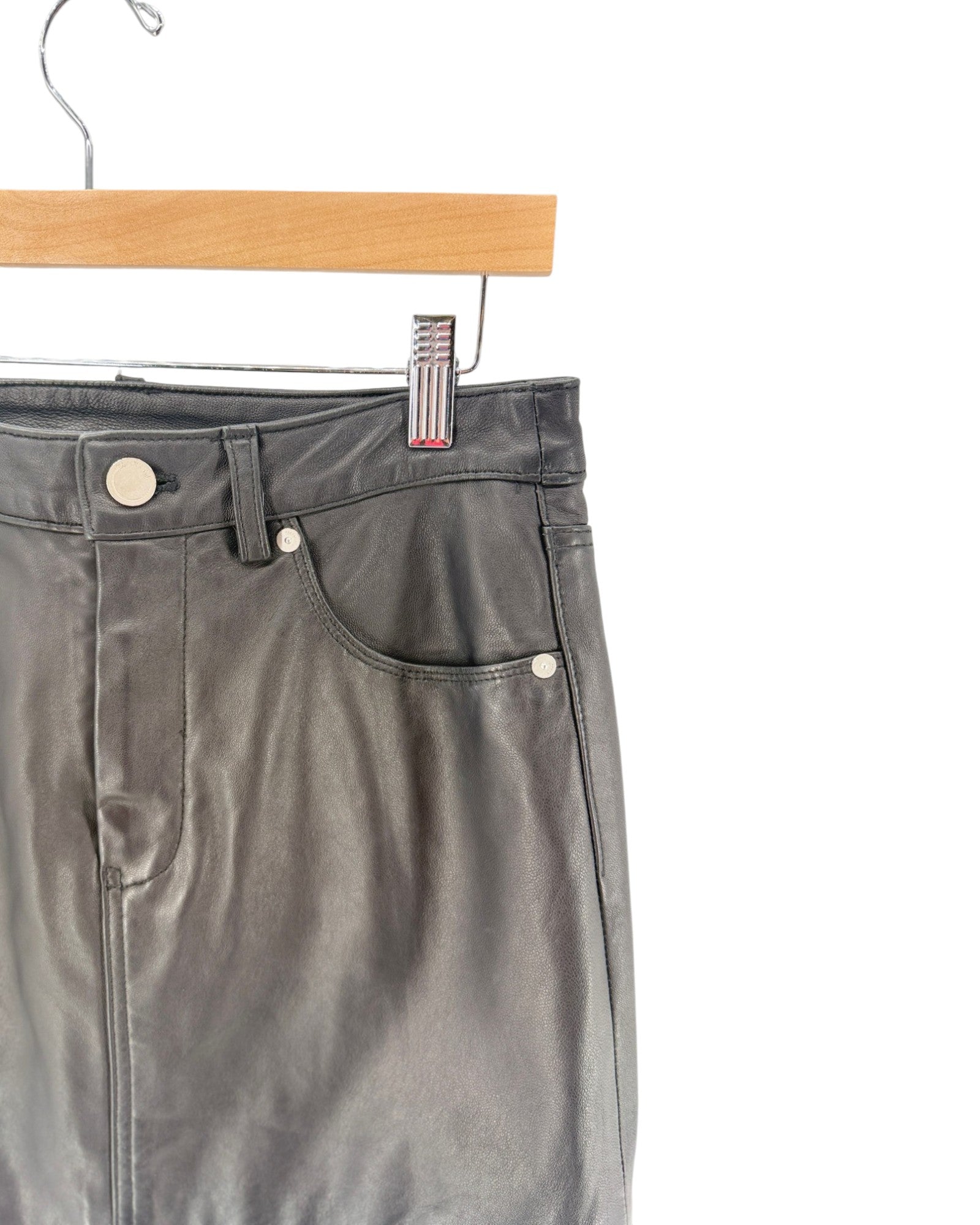 Close-up of dark gray leather pants hanging on a wooden hanger against a white background.