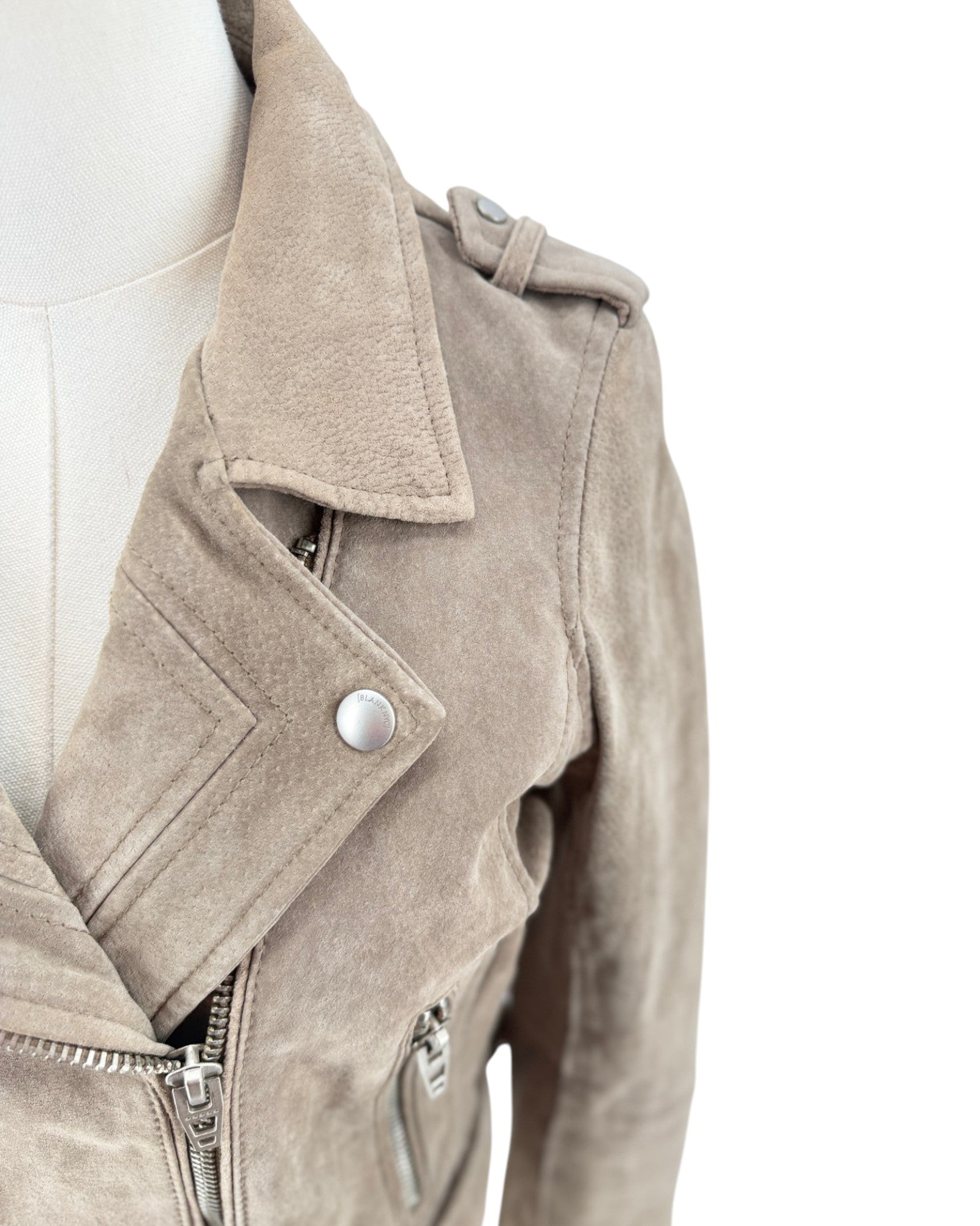 Close-up of a taupe suede motorcycle jacket displayed on a cream mannequin torso against a white background.
