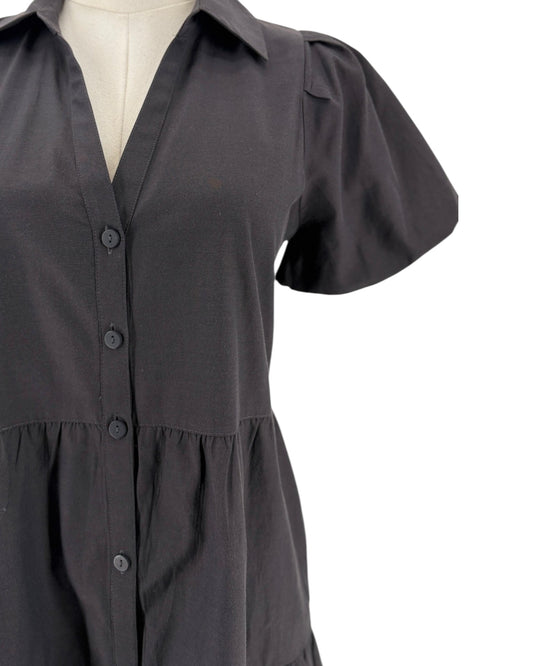 A close-up of a black short-sleeve button-up shirt dress displayed on a cream-colored mannequin torso against a white background.