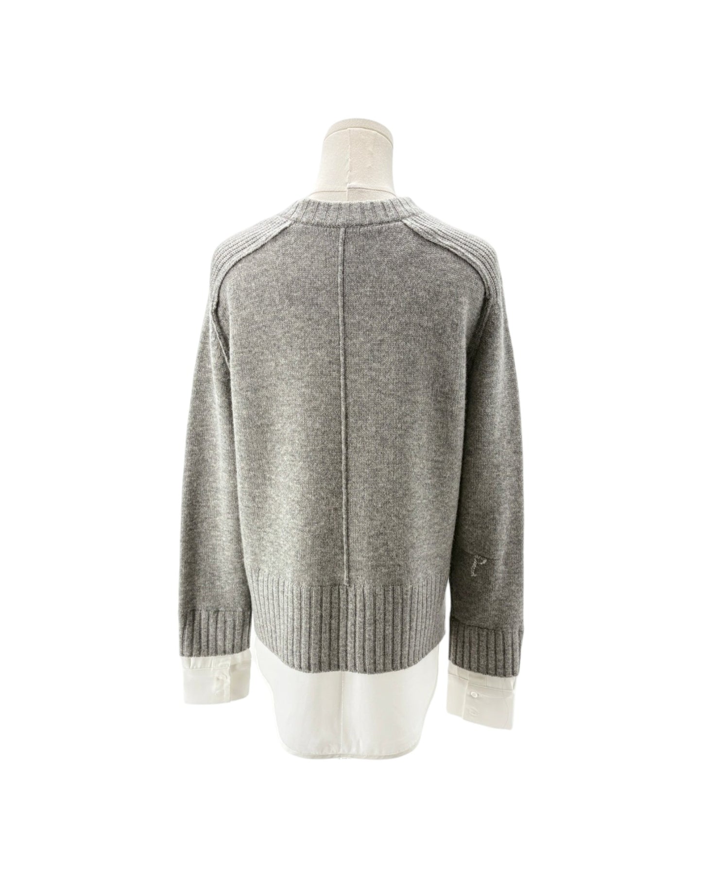 A light gray knit sweater displayed on a mannequin from the back, featuring a contrasting white shirt underneath at the hem and cuffs.