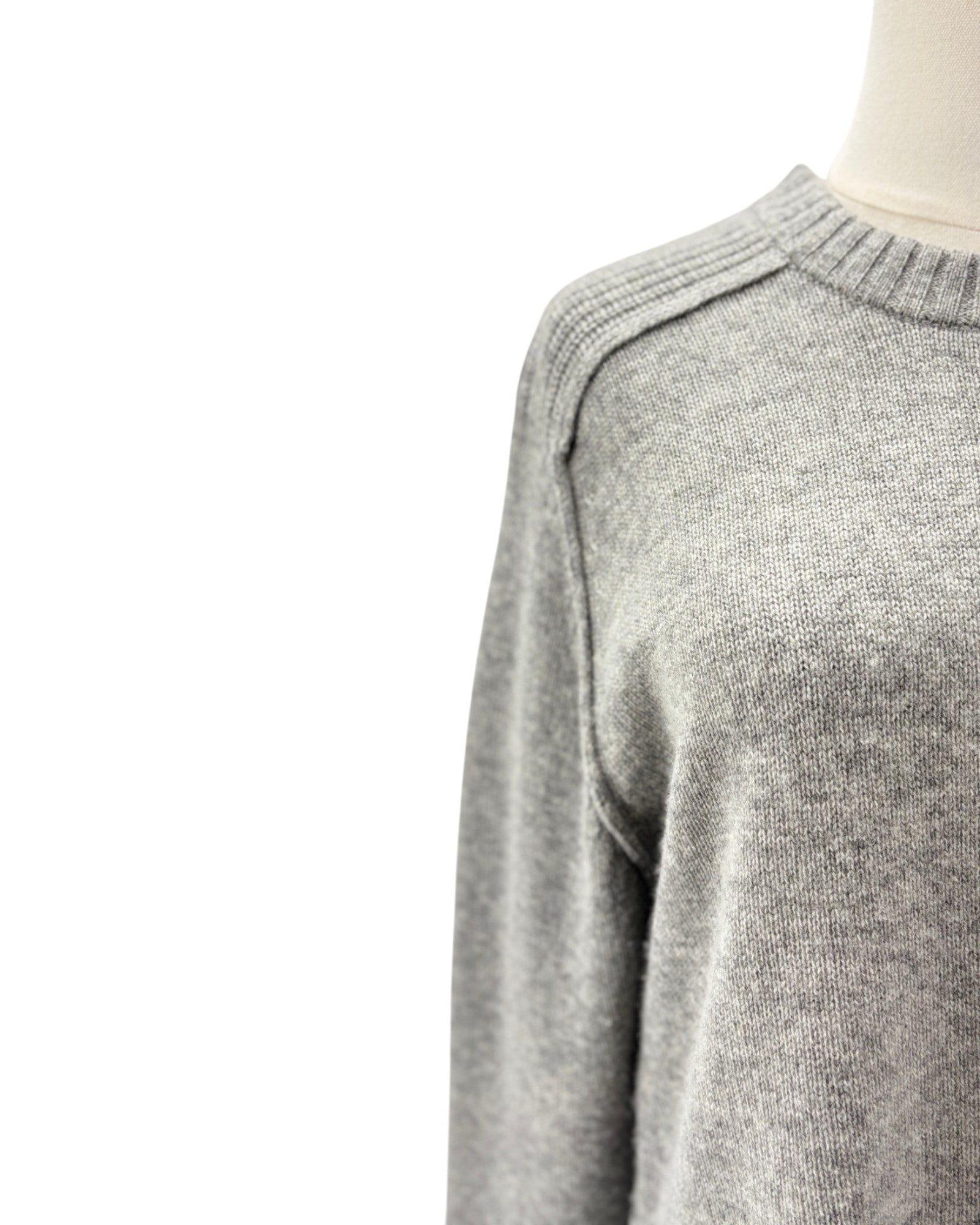 Close-up of a light gray knit sweater on a mannequin torso against a white background.
