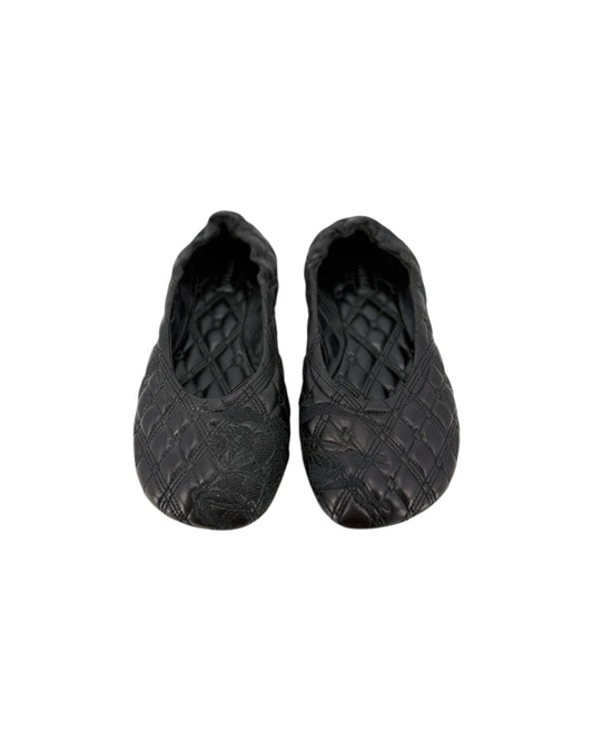 A pair of black quilted slip-on shoes with a textured, embossed pattern, shown against a plain white background.