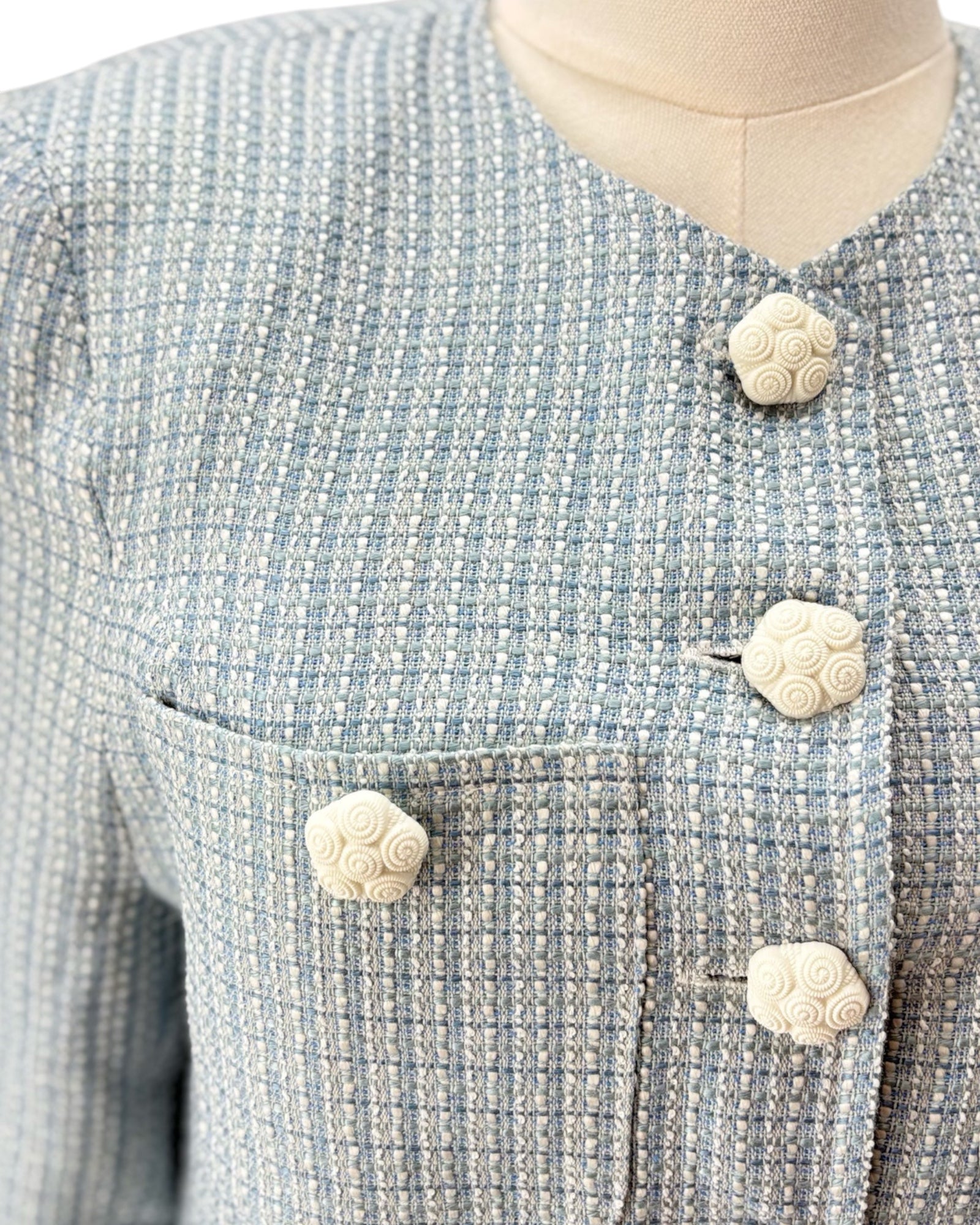 Close-up of a textured blue and gray jacket with decorative buttons on a mannequin.