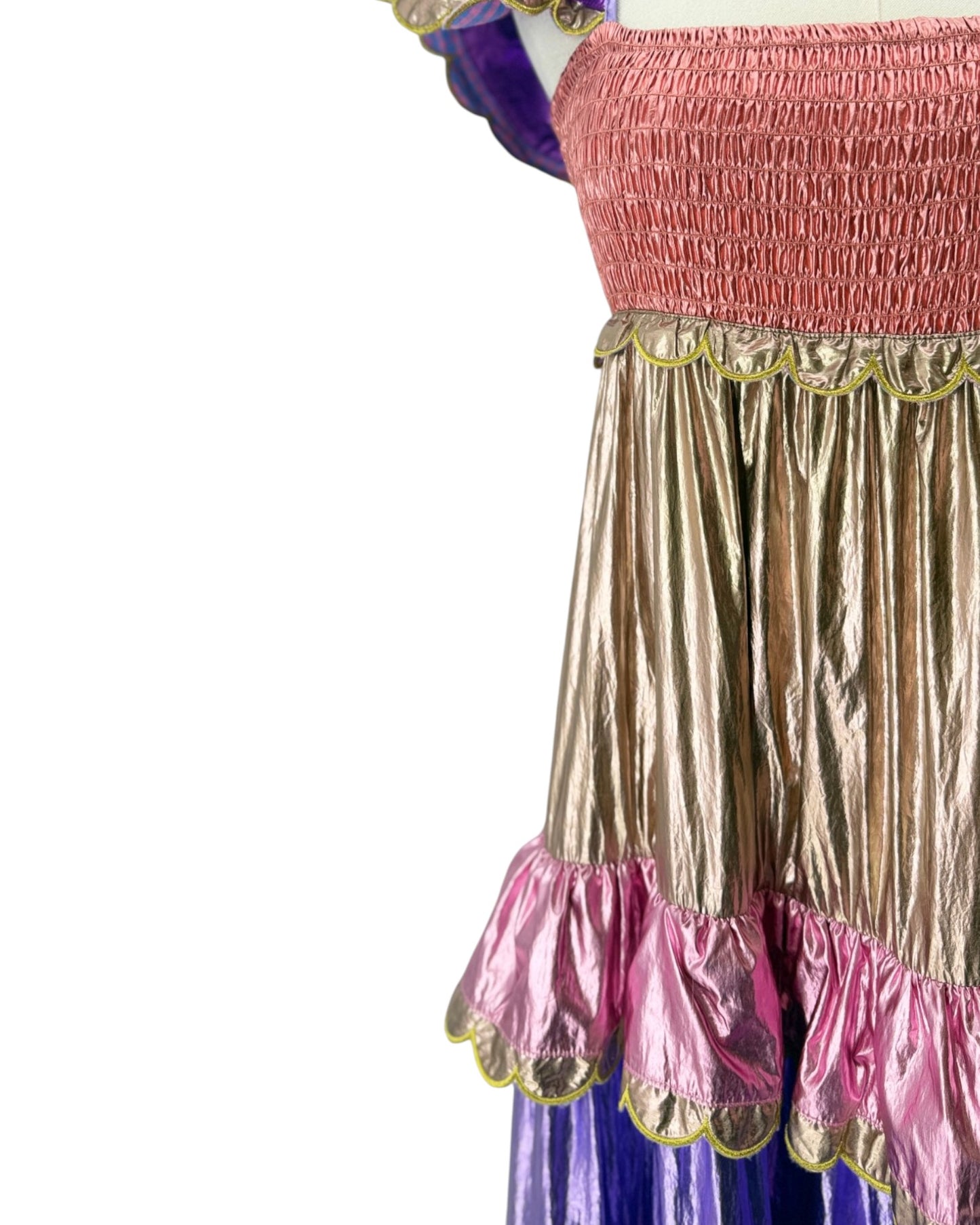 Close-up of a costume dress featuring a metallic gold pleated skirt with pink ruffled trim, a pink smocked bodice, and a purple underlayer visible at the sides and bottom.