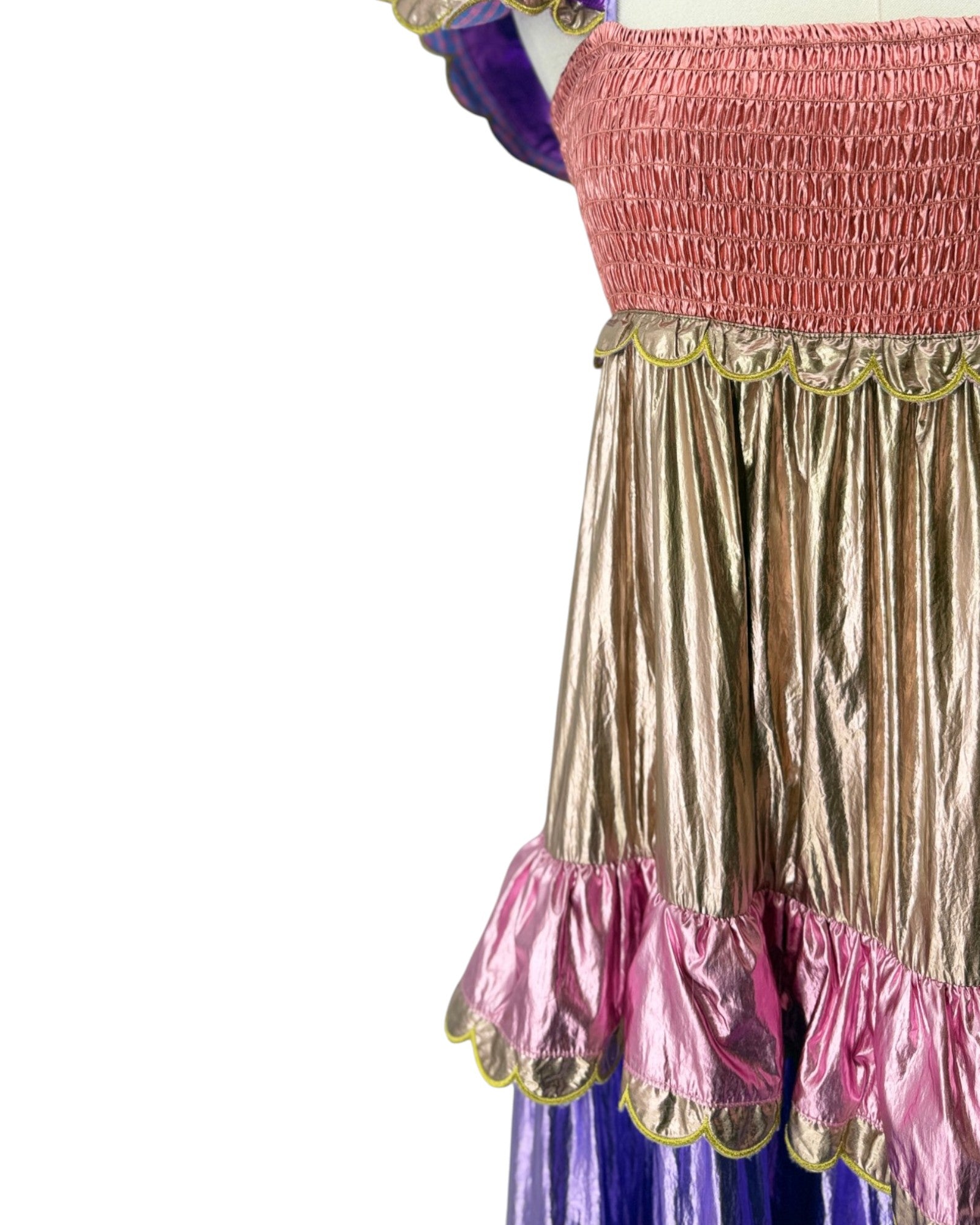 Close-up of a costume dress featuring a metallic gold pleated skirt with pink ruffled trim, a pink smocked bodice, and a purple underlayer visible at the sides and bottom.