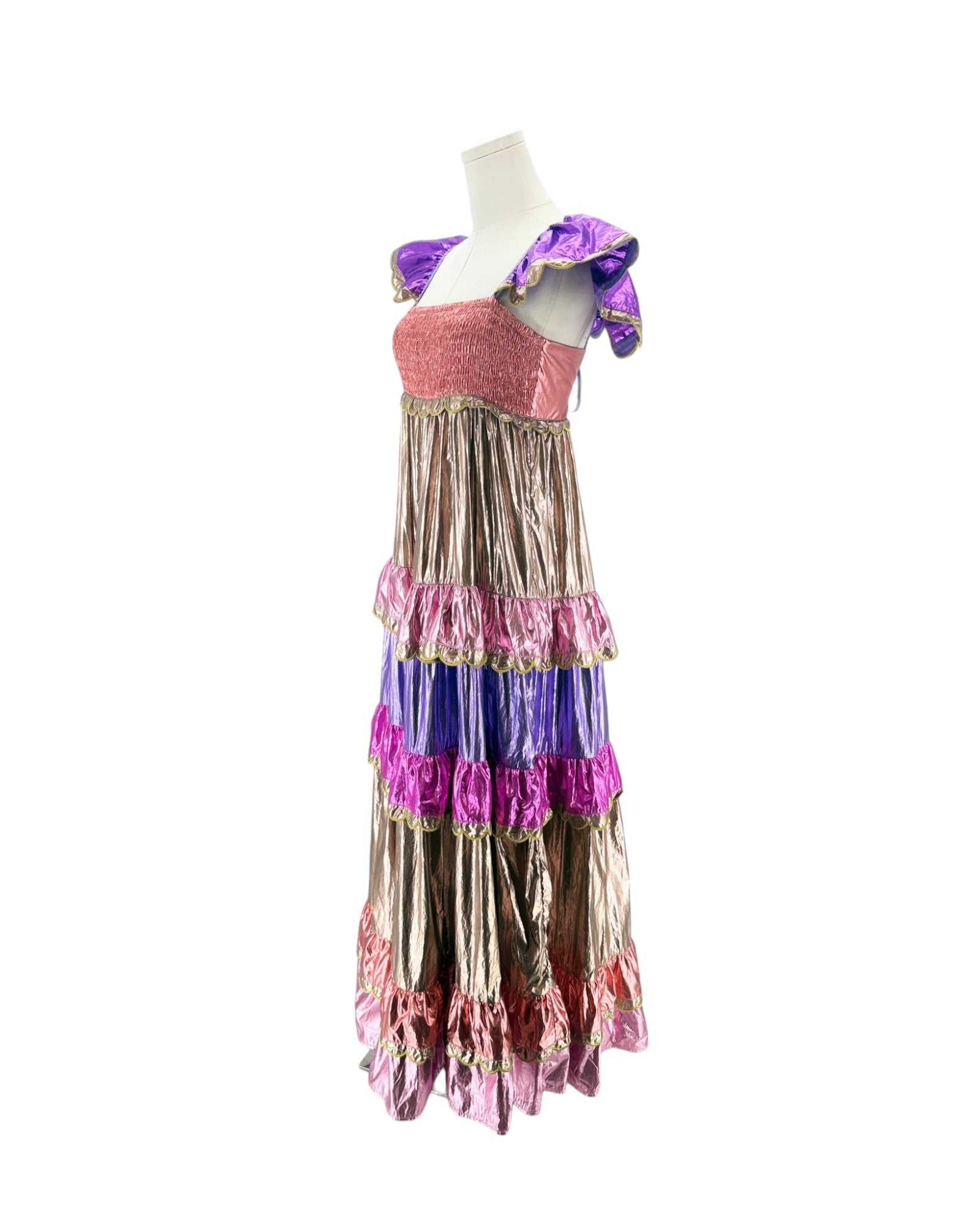 A multi-layered ruffled costume dress displayed on a white mannequin torso against a plain white background. The dress features a textured pink bodice, purple off-the-shoulder straps, and multiple tiers of metallic bronze, purple, and pink ruffles with gold trim.
