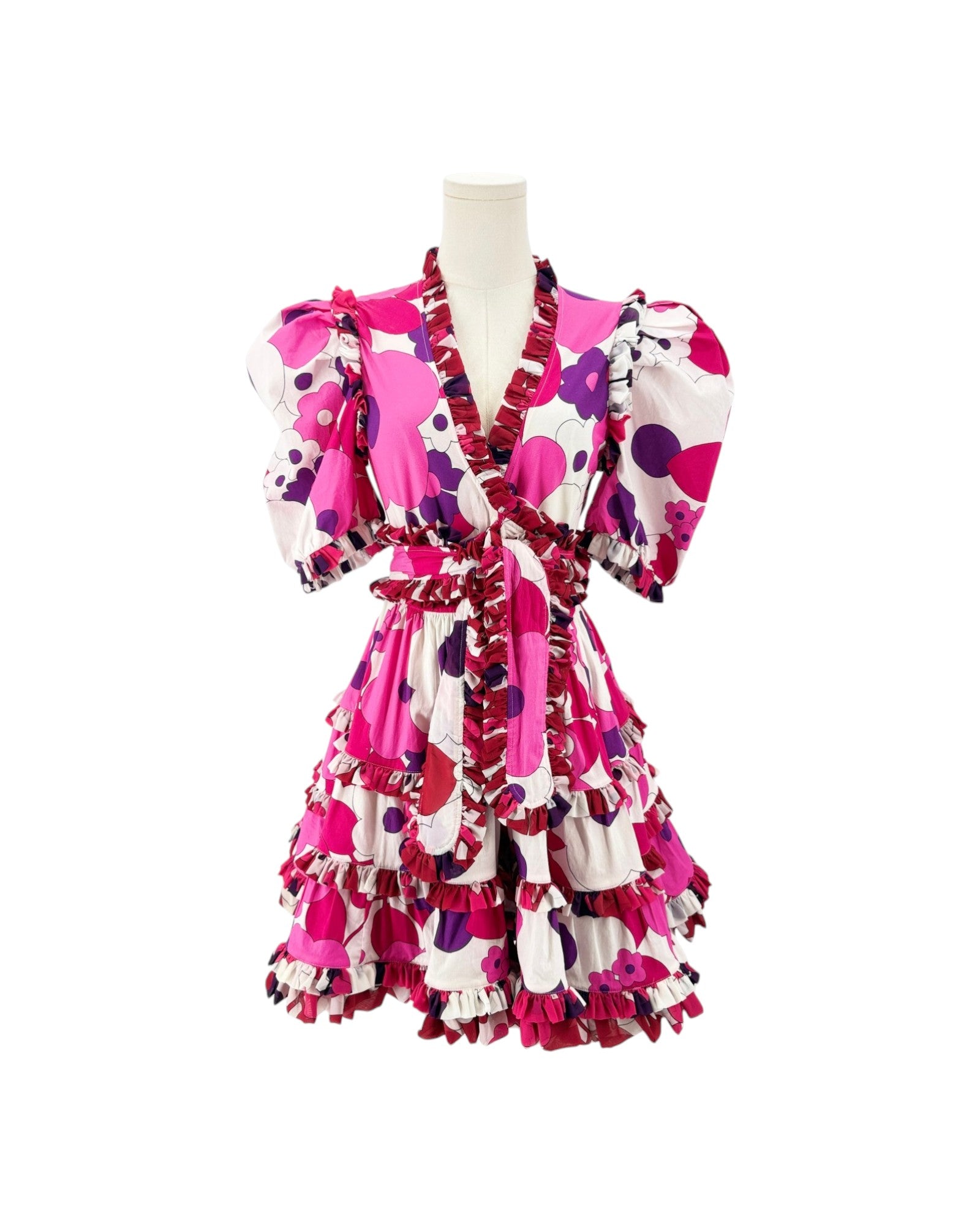 A short ruffled dress displayed on a mannequin torso against a plain white background. The dress has a bold abstract print in hot pink, magenta, purple, and white, with prominent ruffles throughout the bodice, sleeves, and tiered skirt.