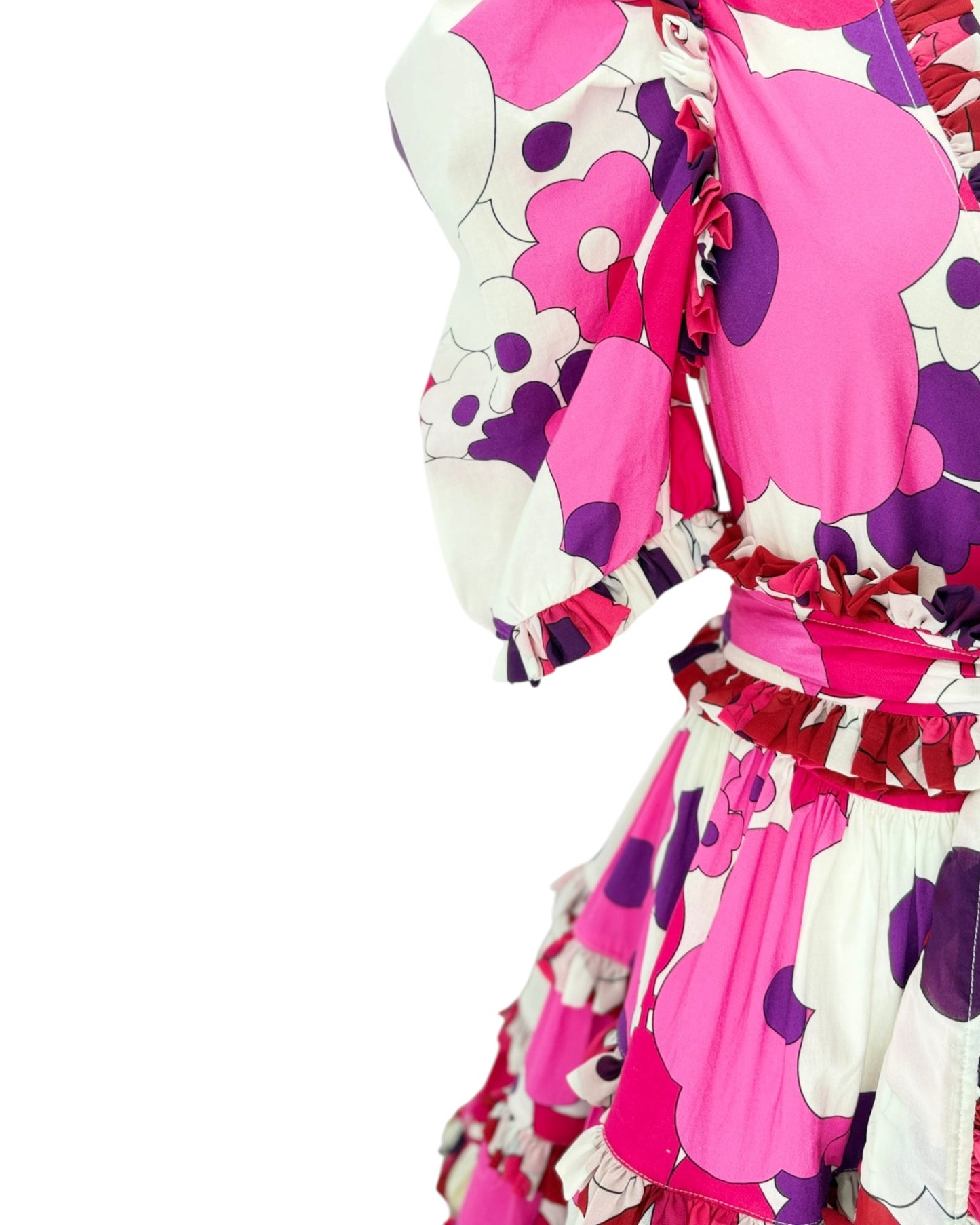 A close-up of a ruffled dress featuring a bold floral pattern in vibrant pink, purple, and white, with puffed sleeves and a ruffled waistband.