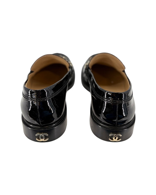 Chanel black patent leather loafer with gold chain detail on a white background