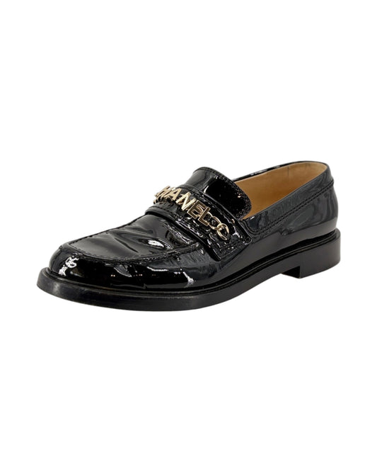 Chanel black patent leather loafer with gold chain detail on a white background