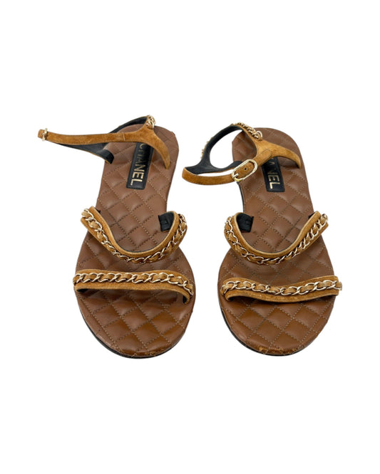 Pair of brown sandals with gold chain details on a white background