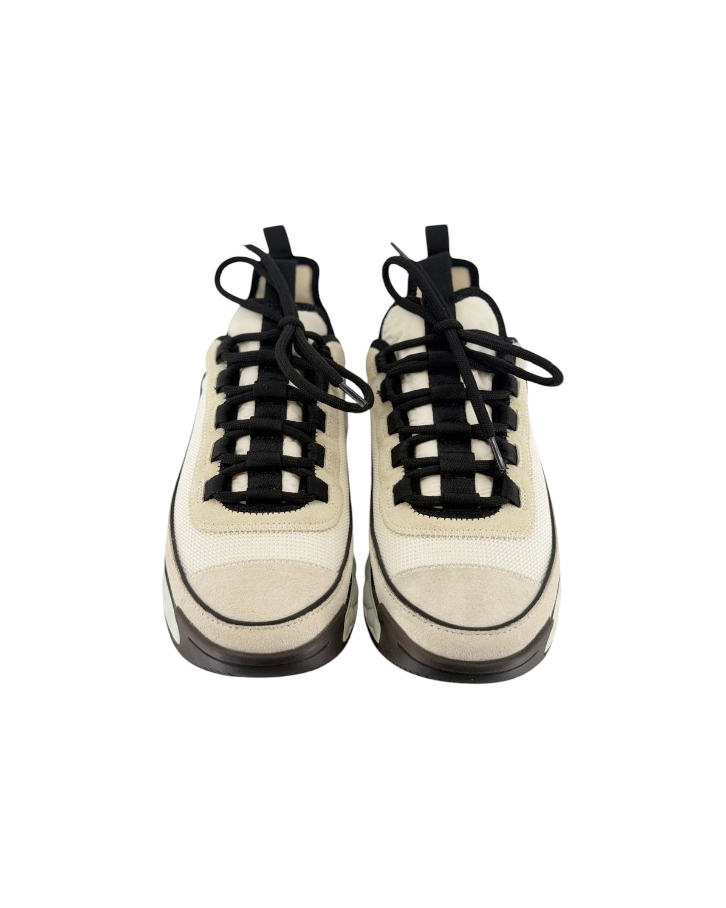A pair of chunky low-top sneakers in off-white and beige suede and mesh, featuring prominent black laces and black soles, shown from a front-facing perspective on a white background.
