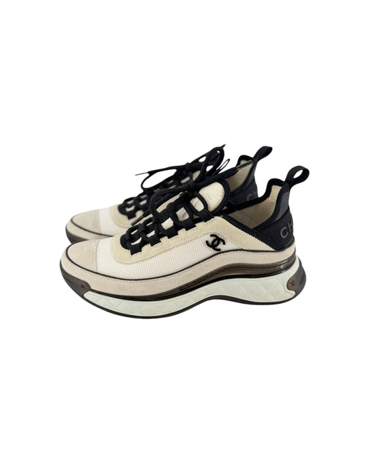 A pair of Chanel chunky sneakers in cream and black, featuring the iconic interlocking CC logo on the side, black laces, and a thick layered sole, shown against a plain white background.