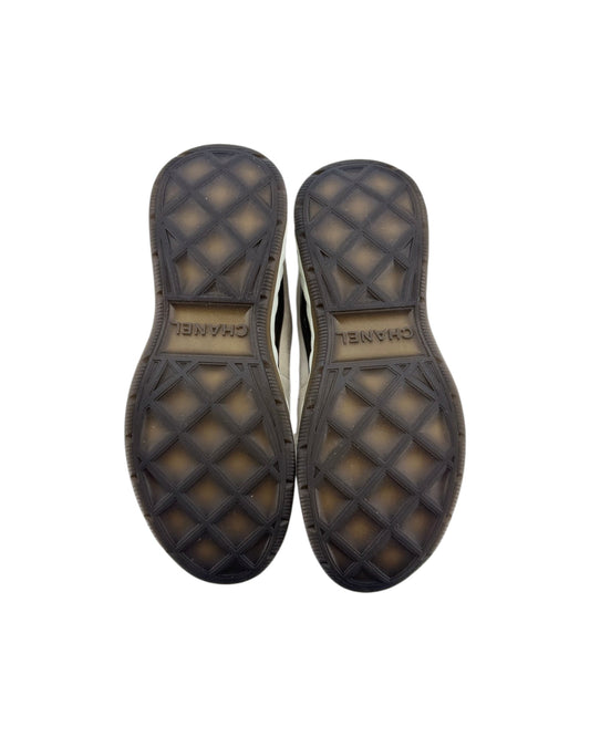 Top-down view of a pair of shoes showing the textured black rubber soles with a diamond pattern and the brand name Chanel printed on the center.
