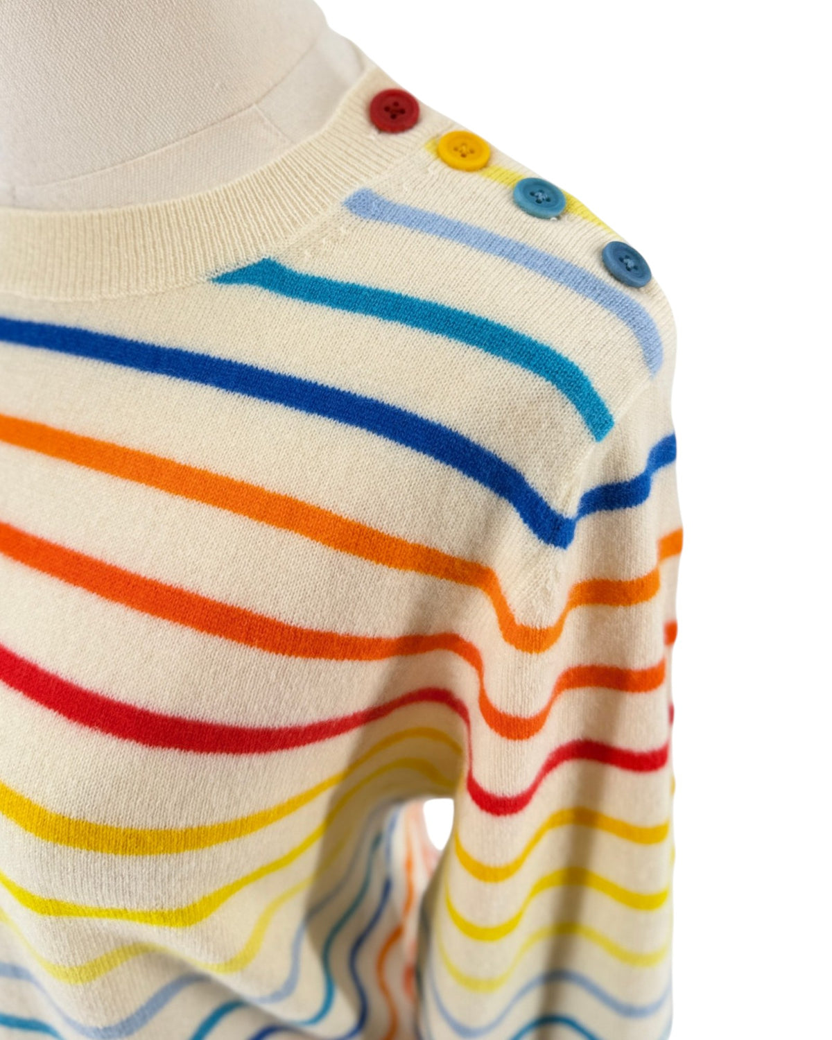 A long-sleeve knit sweater with horizontal rainbow stripes in blue, red, yellow, and orange on an off-white base, displayed on a mannequin torso against a white background.